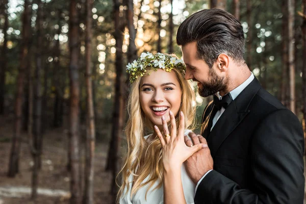 Happy bride in white dress and wreath showing wedding ring on finger in forest — Stock Photo