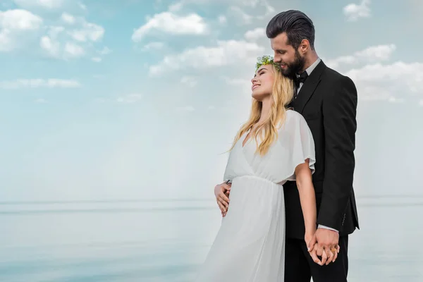 Hochzeitspaar in Anzug und weißem Kleid umarmt sich am Strand — Stockfoto