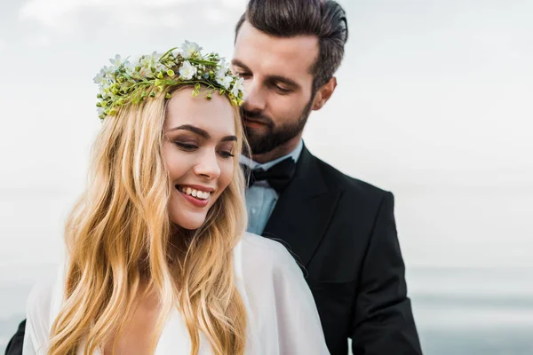 Porträt eines hübschen Bräutigams im Anzug, der attraktive Braut am Strand umarmt — Stockfoto