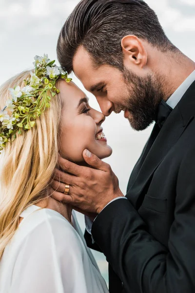 Porträt eines glücklichen Hochzeitspaares in Anzug und weißem Kleid, das sich mit der Nase am Strand berührt — Stockfoto