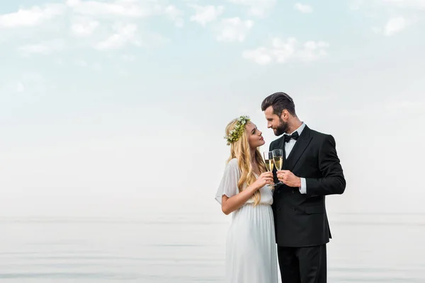 Affectionate wedding couple clinking with glasses of champagne on beach — Stock Photo