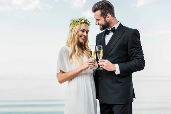 Smiling wedding couple clinking with glasses of champagne on beach — Stock Photo