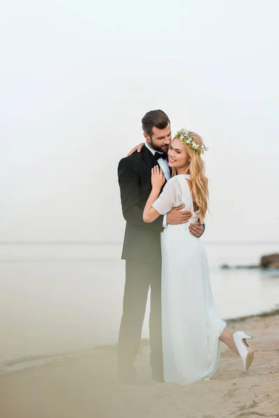 Pareja de boda abrazos en la playa de arena cerca del océano - foto de stock