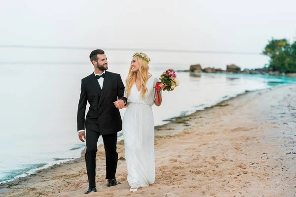 Pareja de boda tomados de la mano y caminando en la playa de arena del océano - foto de stock