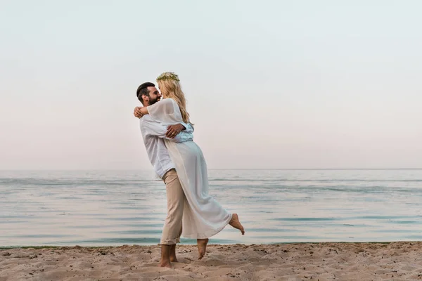 Novia en vestido blanco y novio abrazándose en la playa - foto de stock