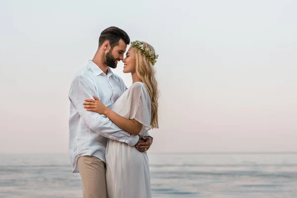 Side view of bride and groom hugging and touching with noses on beach — Stock Photo