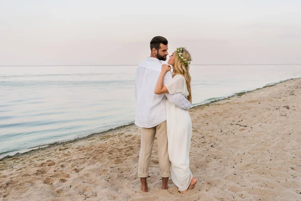 Rear view of bride and groom hugging, walking and going to kiss on beach — Stock Photo