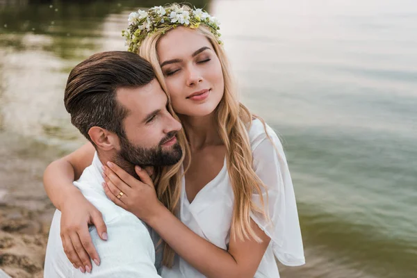 Belle mariée avec les yeux fermés étreignant beau marié sur la plage — Photo de stock