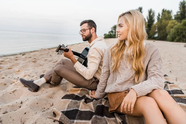 Novio guapo en traje de otoño tocando guitarra acústica para novia en la playa - foto de stock