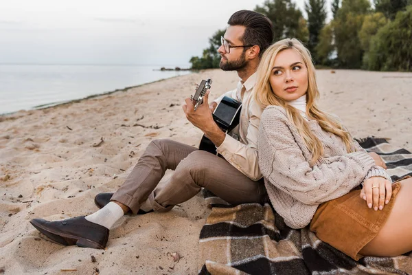 Bello fidanzato in autunno vestito giocare acustica chitarra per fidanzata durante data su spiaggia — Foto stock