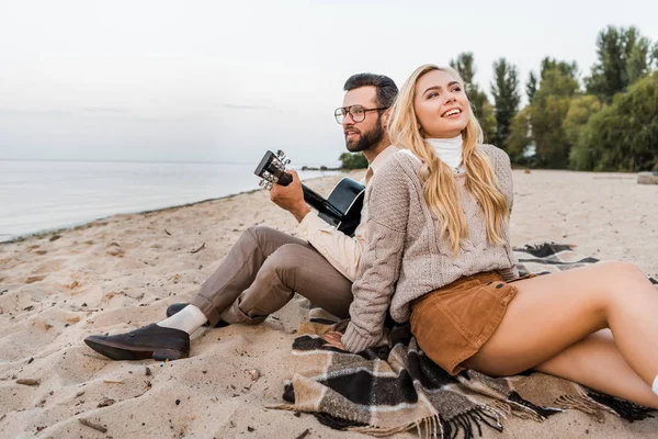 Bonito namorado no outono roupa tocando guitarra acústica para sorrir namorada na praia — Fotografia de Stock