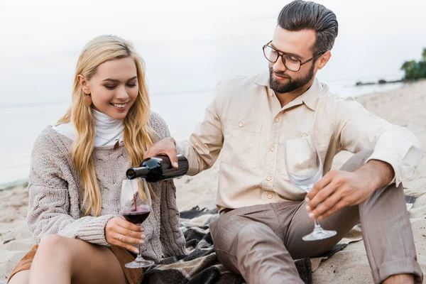 Beau petit ami en tenue d'automne versant du vin rouge dans des verres sur la plage — Photo de stock