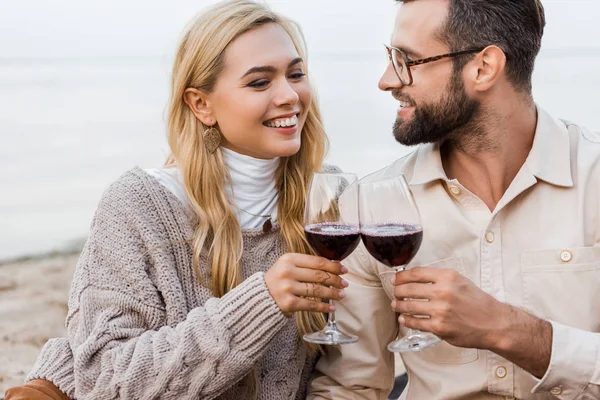 Retrato de novio feliz y novia en traje de otoño tintineo con gafas en la playa - foto de stock