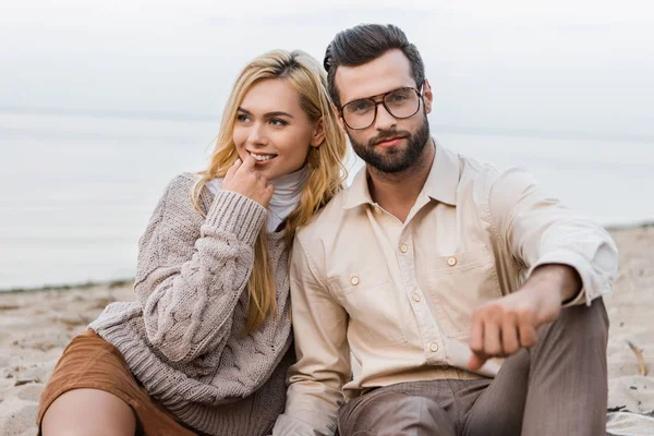 Jolie petite amie et beau petit ami en tenue d'automne assis sur la plage de sable fin — Photo de stock