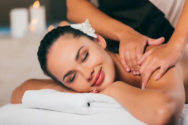 Hermosa mujer con flor en el pelo teniendo masaje en el salón de spa - foto de stock