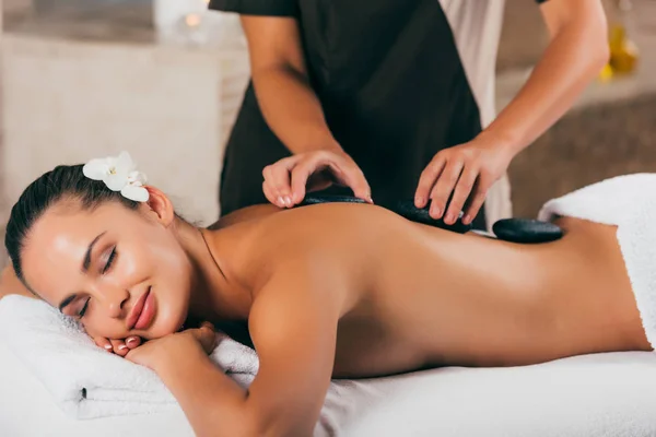 Mujer joven sonriente teniendo terapia de piedra en el salón de spa - foto de stock