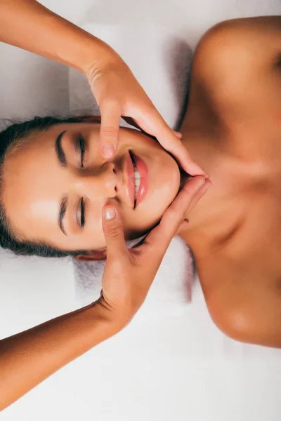 Mujer sonriente relajándose y teniendo masaje facial en el salón de masajes - foto de stock