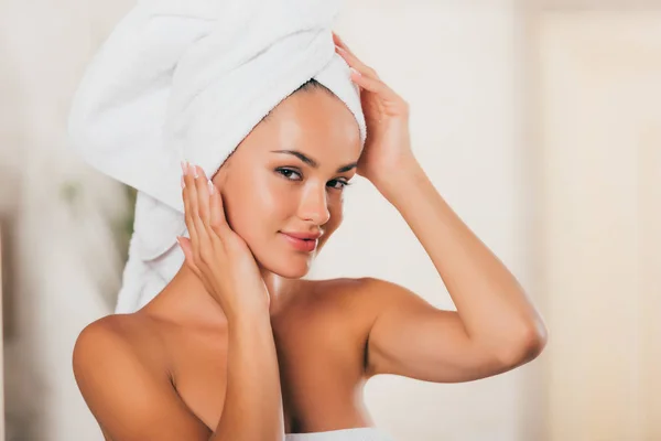 Joven mujer sonriente corrigiendo toalla en la cabeza en el salón de spa - foto de stock