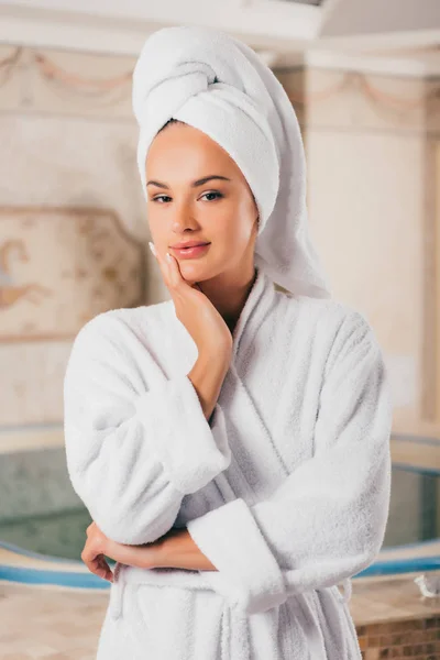 Lächelnde Frau im weißen Frottee-Bademantel mit Handtuch auf dem Kopf im Wellness-Center mit Schwimmbad — Stockfoto