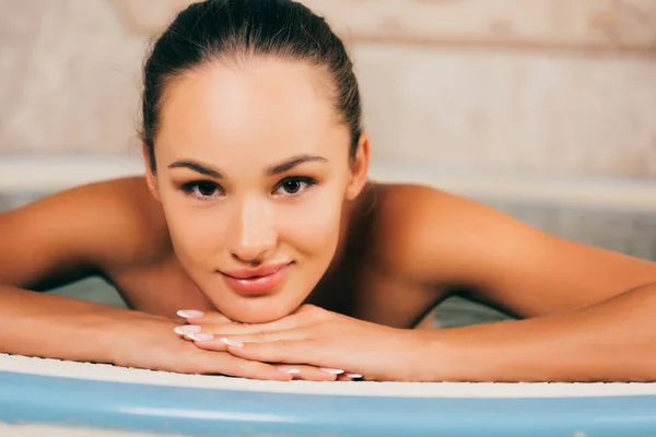 Attractive woman resting in swimming pool in spa salon and looking at camera — Stock Photo