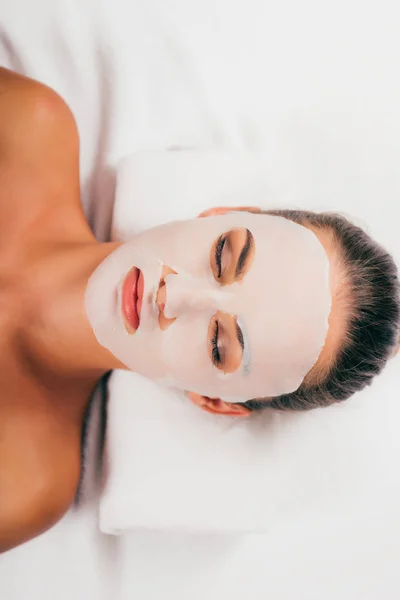 Attrayant jeune femme en masque sur le visage relaxant avec les yeux fermés dans le centre de spa — Photo de stock
