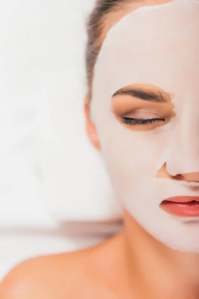 Belle jeune femme masquée sur le visage relaxant avec les yeux fermés dans le salon de spa — Photo de stock