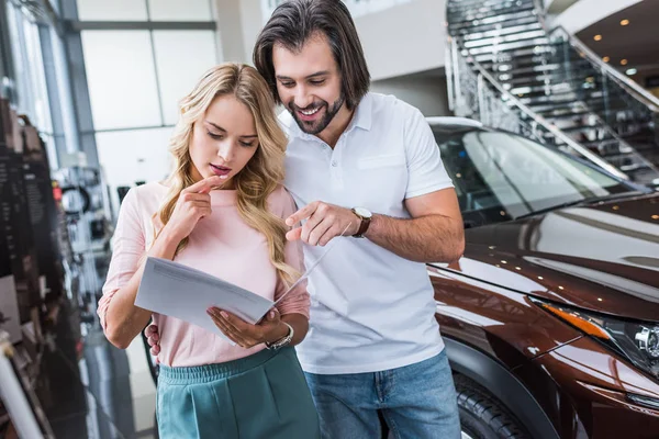 Portrait of couple with catalog choosing car at dealership salon — Stock Photo