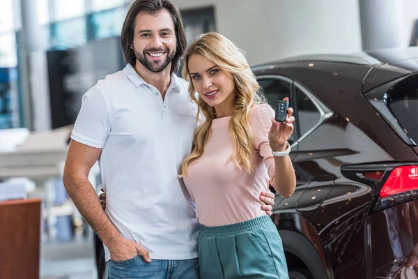 Retrato de casal sorridente com chave de carro em pé no salão de concessionárias — Fotografia de Stock