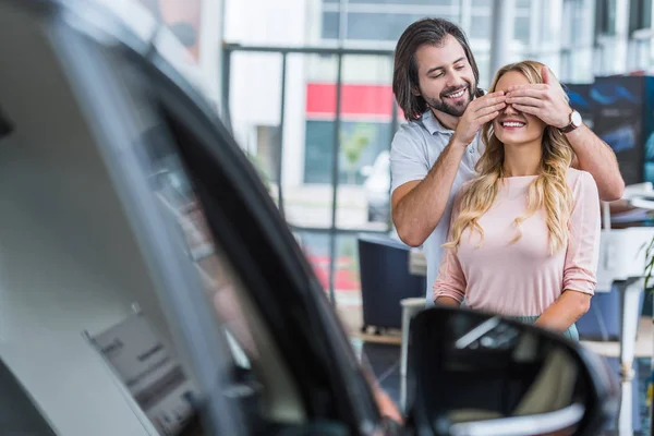 Homme souriant petite amie surprenante avec nouvelle voiture au salon de concession — Photo de stock