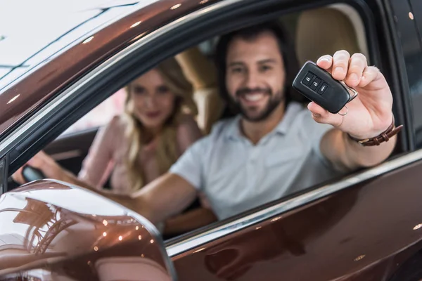 Selective focus of smiling couple with car key sitting in new car at dealership salon — Stock Photo