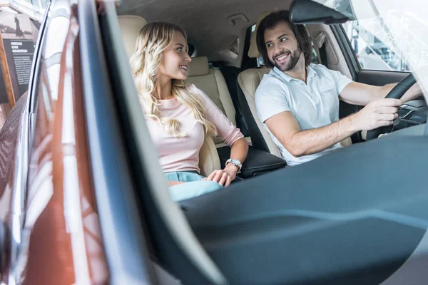 Sonriente pareja sentado en nuevo automóvil en salón de concesionarios - foto de stock