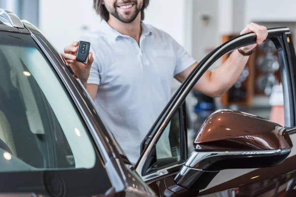 Schnappschuss von lächelndem Mann mit Autoschlüssel, der vor Neuwagen im Autohaus steht — Stockfoto