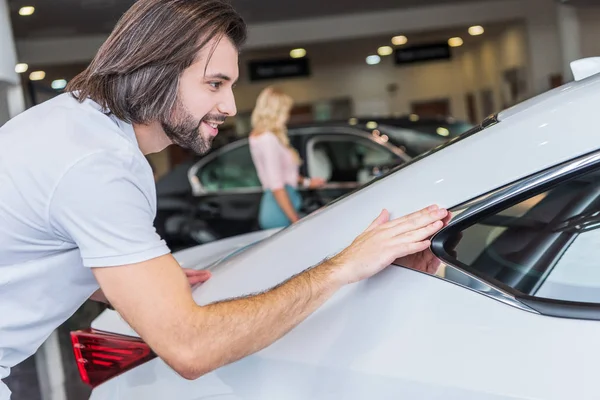 Enfoque selectivo del hombre que comprueba el automóvil con la novia en el fondo en el salón de concesionarios - foto de stock