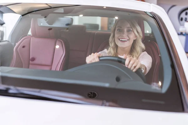 Retrato de mulher feliz sentado em carro novo no salão de concessionárias — Fotografia de Stock