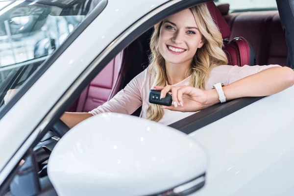 Porträt einer lächelnden Frau mit Autoschlüssel in der Hand, die in einem Neuwagen im Autohaus-Salon sitzt — Stockfoto