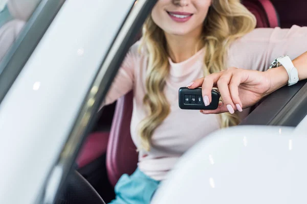 Vista parcial de la mujer con la llave del coche en la mano sentado en el coche nuevo en el salón de concesionarios - foto de stock