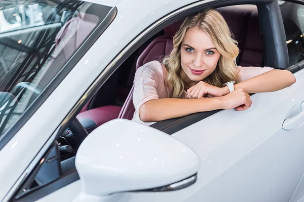 Portrait of young woman looking at camera while sitting in new car in dealership salon — Stock Photo