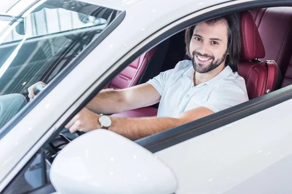 Homme barbu souriant assis dans une voiture neuve pour un essai routier dans le salon de concession — Photo de stock