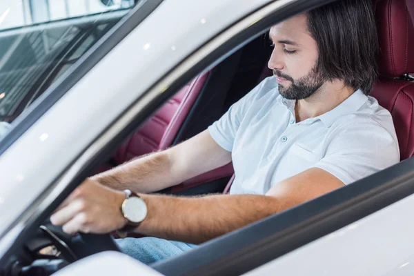 Uomo barbuto seduto in auto nuova per test drive nel salone di concessionaria — Foto stock