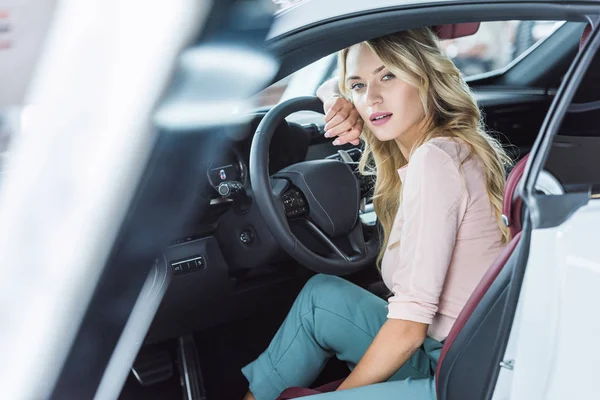 Вид сбоку молодой застенчивой женщины, сидящей в новом автомобиле в дилерском салоне — стоковое фото