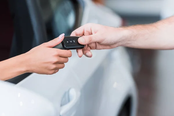 Cropped shot of man giving car key to woman at dealership salon — Stock Photo