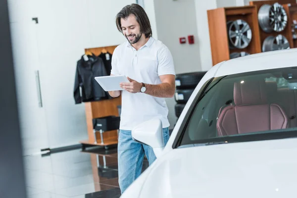 Homme souriant utilisant tablette numérique dans les mains au salon de concession — Photo de stock