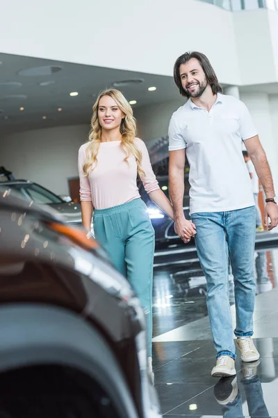 Happy couple holding hands while walking at dealership salon — Stock Photo