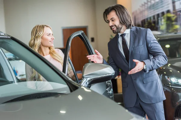 Vendedor de ropa formal recomendando automóvil a la mujer en el salón de concesionarios - foto de stock