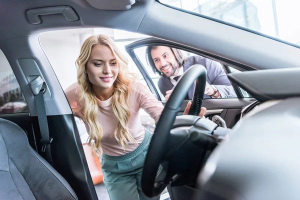 Seller in formal wear recommending automobile to woman at dealership salon — Stock Photo
