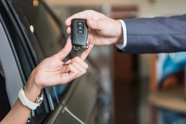 Cropped shot of dealership salon seller giving car key to woman in auto salon — Stock Photo