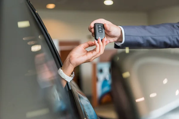 Cropped shot of dealership salon seller giving car key to woman in auto salon — Stock Photo