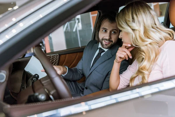 Dealership salon seller and female customer sitting in car in auto salon — Stock Photo