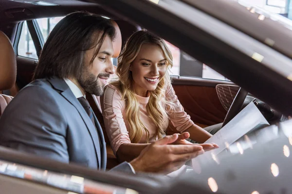 Concessionaria venditore salone e sorridente cliente femminile seduto in auto in salone auto — Foto stock