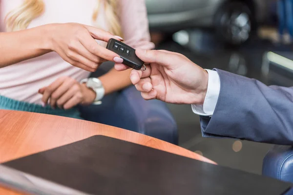 Cropped shot of dealership salon seller giving car key to woman in auto salon — Stock Photo